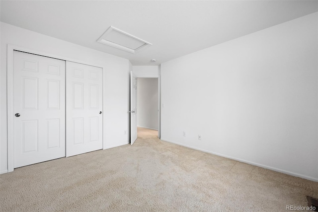 unfurnished bedroom featuring attic access, light colored carpet, and a closet