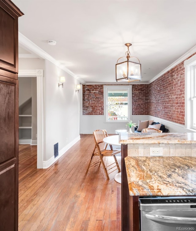 dining room with brick wall, a chandelier, light wood-style flooring, and visible vents
