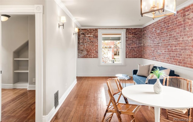 living area with brick wall, ornamental molding, wainscoting, and hardwood / wood-style floors