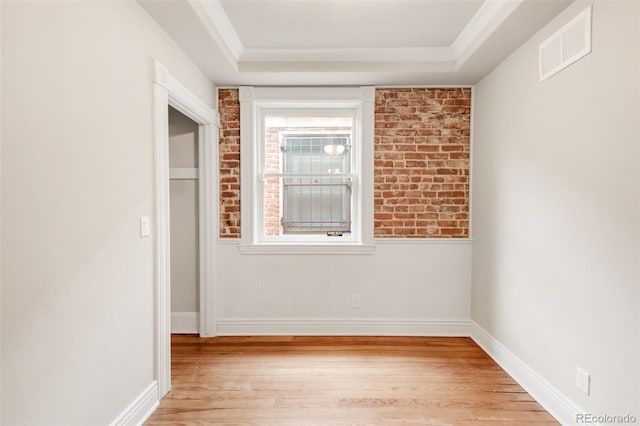 empty room featuring baseboards, visible vents, light wood-style flooring, and a raised ceiling