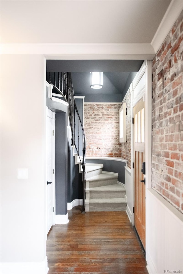 stairs with a wainscoted wall, brick wall, and wood finished floors