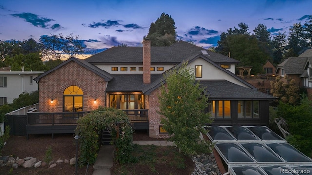 rear view of property with stucco siding, a chimney, a deck, and brick siding