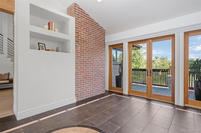 doorway to outside with a healthy amount of sunlight, built in shelves, vaulted ceiling, and dark tile patterned flooring