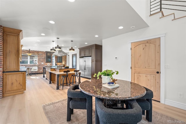 dining space featuring baseboards, brick wall, stairway, light wood-type flooring, and recessed lighting