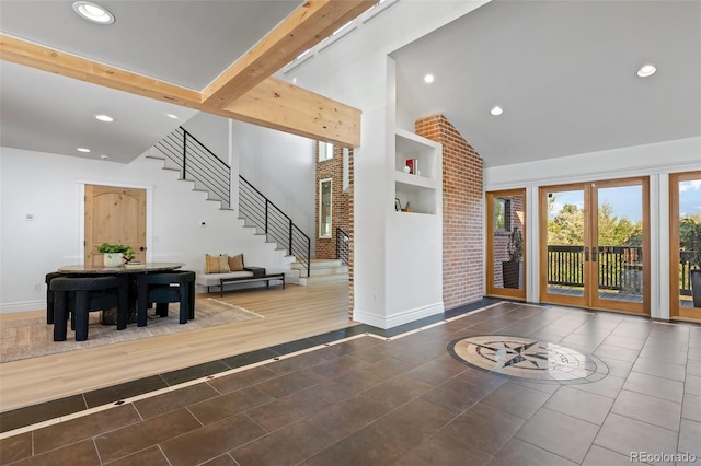 entrance foyer with french doors, stairway, brick wall, high vaulted ceiling, and tile patterned flooring