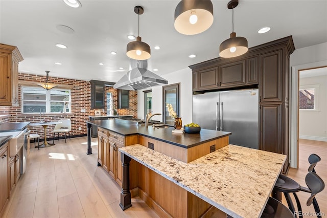 kitchen with stainless steel built in fridge, brick wall, island range hood, a large island with sink, and a kitchen bar