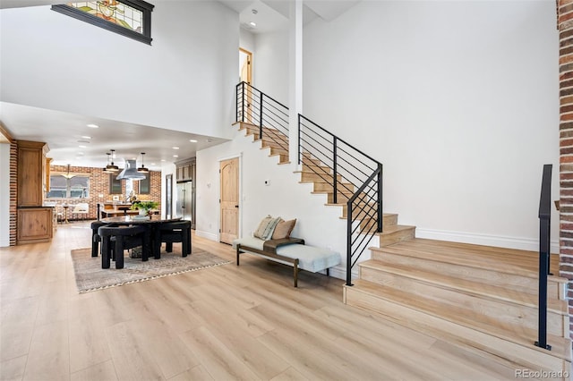 foyer featuring light wood finished floors, recessed lighting, a towering ceiling, baseboards, and stairs