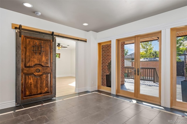 doorway to outside featuring baseboards, dark tile patterned flooring, a barn door, and recessed lighting