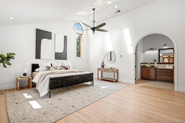 bedroom featuring arched walkways, vaulted ceiling with skylight, ensuite bathroom, visible vents, and light wood-style floors