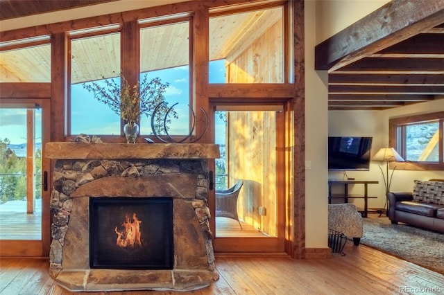 interior space featuring a stone fireplace, plenty of natural light, beamed ceiling, and wood-type flooring