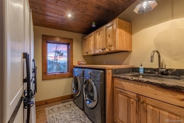 clothes washing area with washer and clothes dryer, cabinets, sink, light wood-type flooring, and wood ceiling