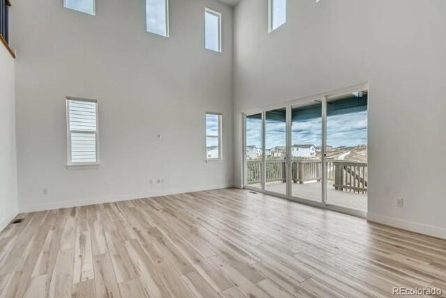 unfurnished living room featuring a high ceiling, light wood finished floors, plenty of natural light, and baseboards