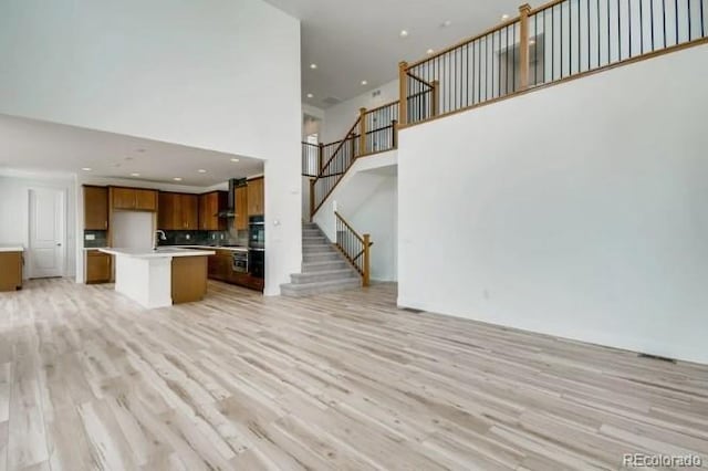 unfurnished living room featuring a high ceiling, light wood finished floors, stairway, a sink, and recessed lighting