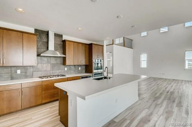 kitchen with wall chimney exhaust hood, appliances with stainless steel finishes, light countertops, light wood-style flooring, and backsplash