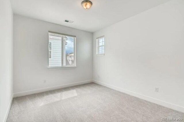 spare room featuring light colored carpet and baseboards