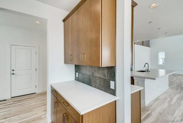 kitchen with light wood-style flooring, tasteful backsplash, light countertops, a sink, and brown cabinets