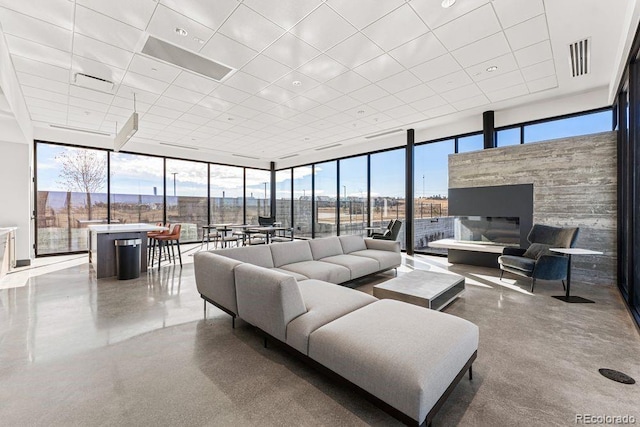 living area featuring a wall of windows, a drop ceiling, plenty of natural light, and a fireplace