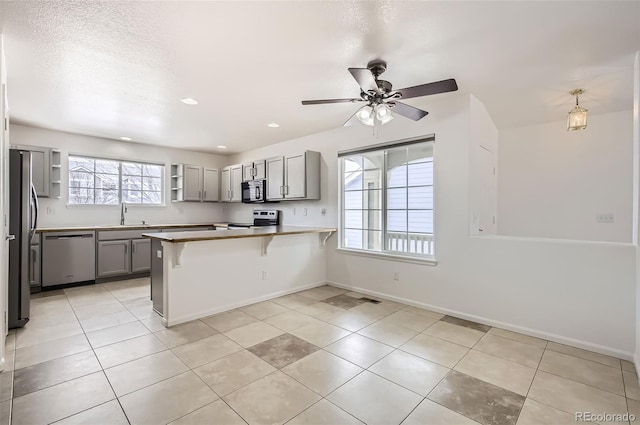 kitchen featuring appliances with stainless steel finishes, a breakfast bar, a peninsula, gray cabinetry, and a sink