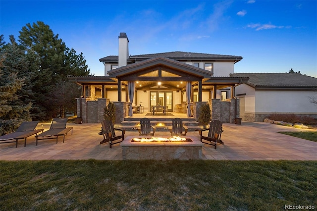 back of house featuring stucco siding, a patio, stone siding, a fire pit, and a chimney