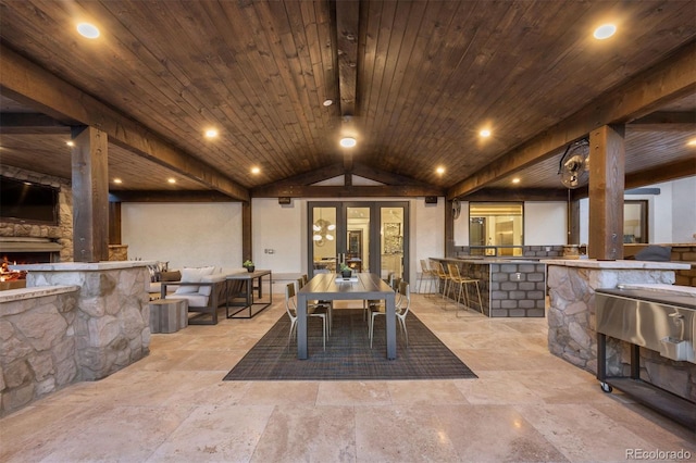 interior space with wood ceiling, stone tile floors, lofted ceiling, and a warm lit fireplace