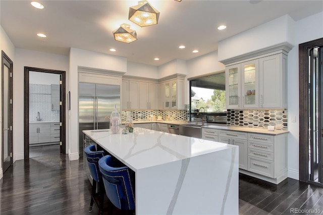 kitchen featuring dark wood-style flooring, a kitchen breakfast bar, an island with sink, stainless steel appliances, and a sink