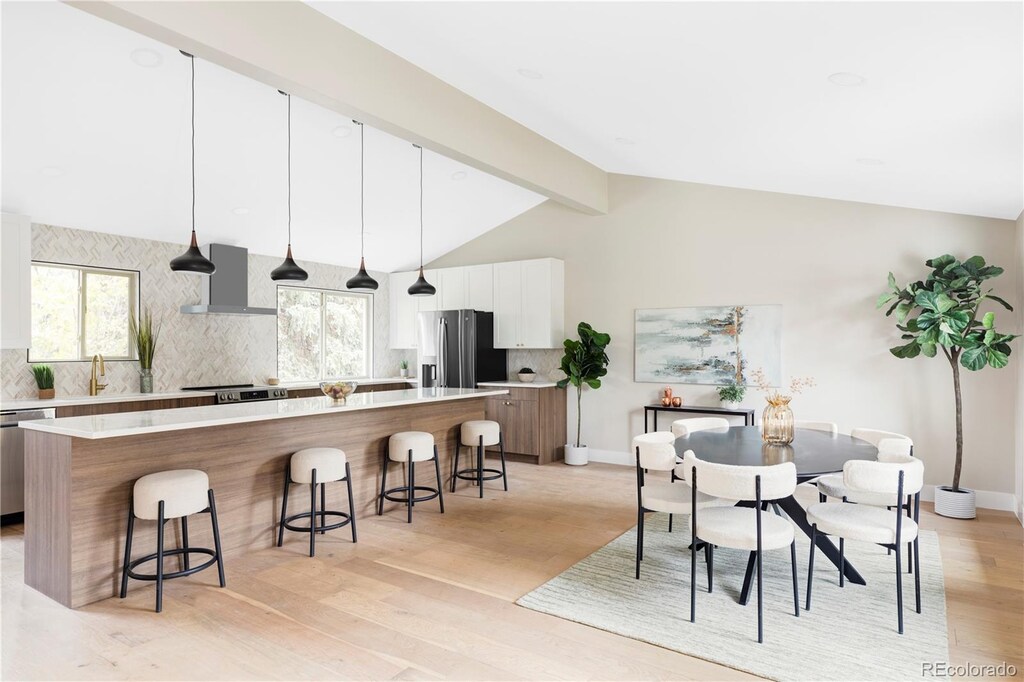 kitchen featuring white cabinetry, a center island, wall chimney range hood, pendant lighting, and appliances with stainless steel finishes