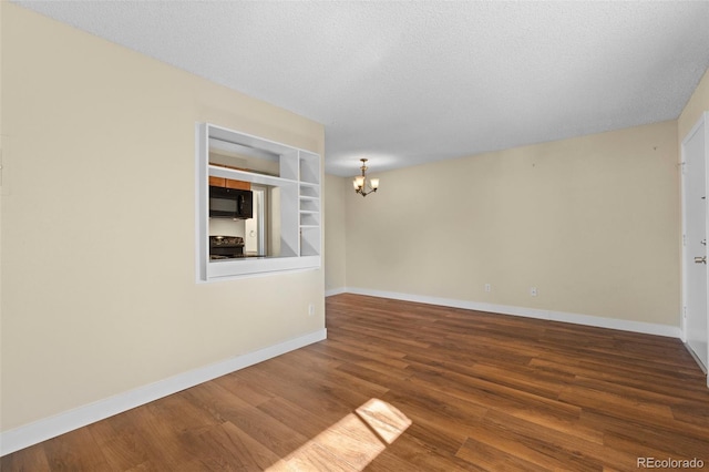 spare room with hardwood / wood-style floors, a textured ceiling, an inviting chandelier, and built in features