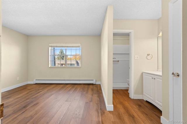 unfurnished bedroom with a spacious closet, light wood-type flooring, a textured ceiling, and a baseboard radiator