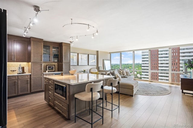 3100 E Cherry Creek S Drive 1403, Denver, CO 80209 - kitchen featuring stainless steel microwave, a breakfast bar area, tasteful backsplash, wood finished floors, and glass insert cabinets