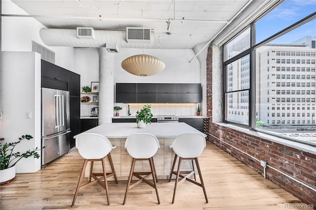 2000 Arapahoe St Unit 503, Denver, CO 80205 - kitchen featuring appliances with stainless steel finishes, brick wall, dark cabinets, light wood-style flooring, and a breakfast bar area