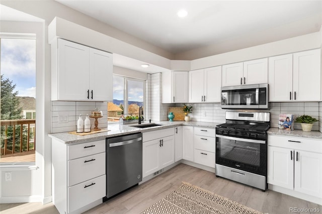 kitchen featuring sink, stainless steel appliances, light hardwood / wood-style flooring, backsplash, and white cabinets