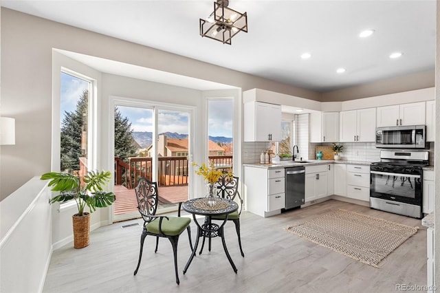 kitchen with appliances with stainless steel finishes, tasteful backsplash, an inviting chandelier, light hardwood / wood-style flooring, and white cabinets