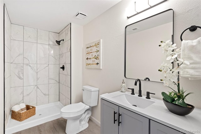 bathroom featuring tiled shower, vanity, wood-type flooring, and toilet