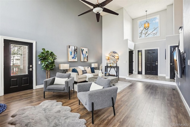 living area featuring baseboards, ceiling fan, wood finished floors, and a towering ceiling