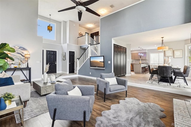 living area with a ceiling fan, a towering ceiling, stairway, baseboards, and light wood-style floors