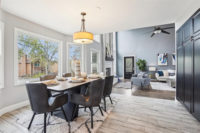 dining area with baseboards, a fireplace, a ceiling fan, and light wood-type flooring