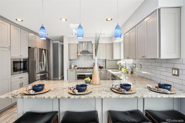 kitchen featuring stainless steel appliances, light stone counters, a sink, and wall chimney exhaust hood