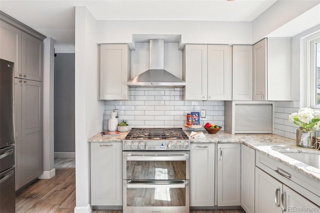 kitchen featuring baseboards, wall chimney range hood, gray cabinets, backsplash, and stainless steel appliances