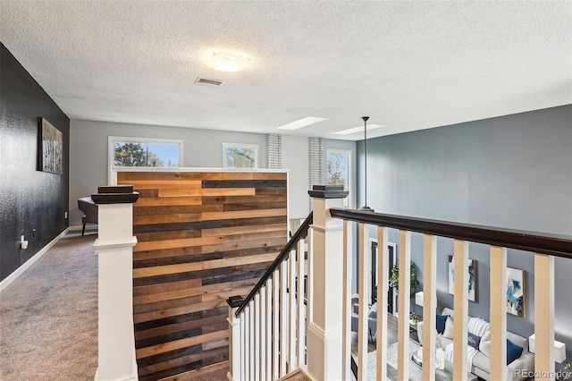 staircase featuring a textured ceiling, visible vents, a skylight, baseboards, and carpet flooring