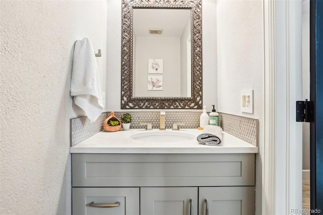 bathroom featuring vanity, decorative backsplash, a textured wall, and visible vents