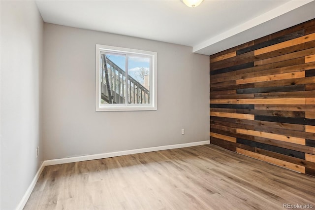 spare room featuring wooden walls, baseboards, and wood finished floors