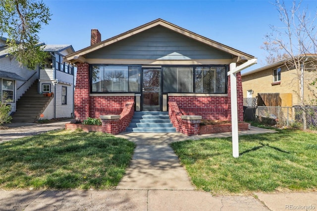 bungalow-style home with a front lawn, fence, a chimney, brick siding, and entry steps