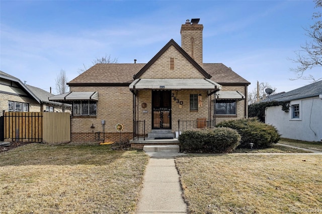 view of front of home with a front yard, fence, a shingled roof, a chimney, and brick siding