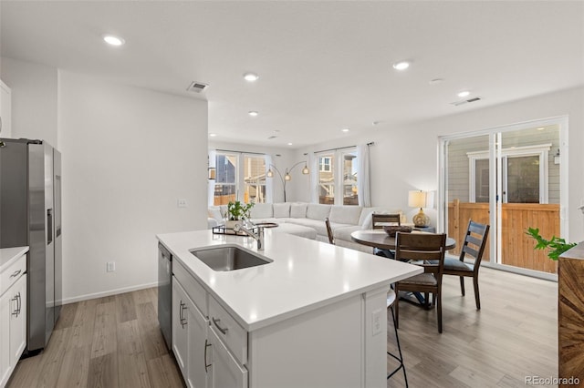 kitchen featuring sink, appliances with stainless steel finishes, white cabinetry, a center island with sink, and light wood-type flooring