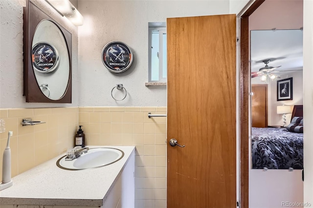 6436 Otis St, Arvada, CO 80003 - bathroom featuring a ceiling fan, vanity, tile walls, and a wainscoted wall