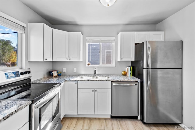 kitchen with white cabinets, light stone countertops, light hardwood / wood-style flooring, sink, and stainless steel appliances