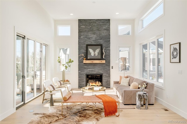 living area featuring a high ceiling, a fireplace, wood finished floors, and baseboards