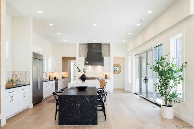 8230 W Tennessee Ct, Lakewood, CO 80226 - kitchen with premium range hood, appliances with stainless steel finishes, decorative backsplash, light wood-style flooring, and white cabinets
