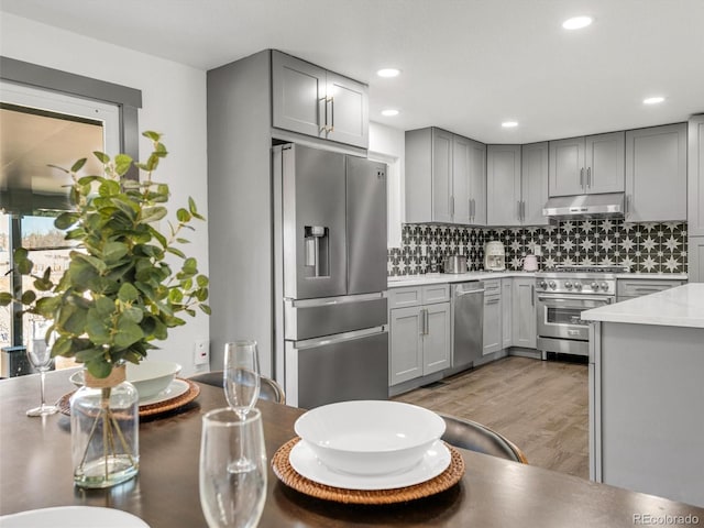 kitchen featuring under cabinet range hood, stainless steel appliances, light countertops, backsplash, and gray cabinets