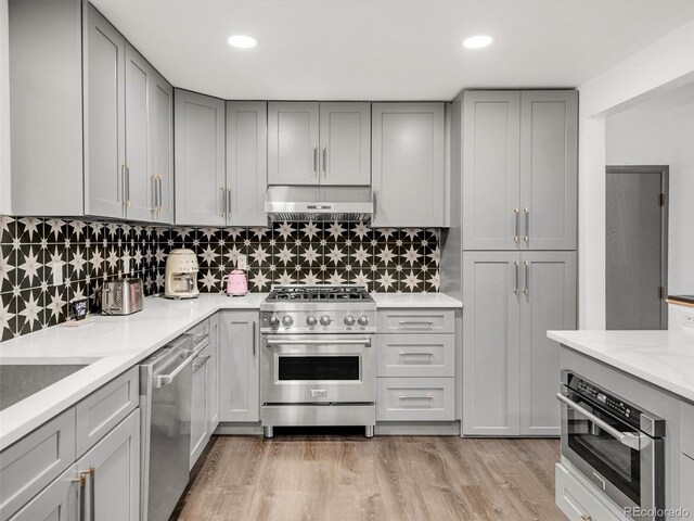 kitchen with appliances with stainless steel finishes, light wood-style floors, under cabinet range hood, and gray cabinetry